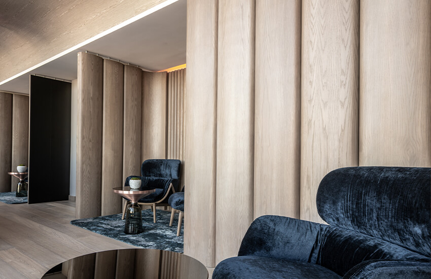 Modern lounge with tall wood panels, velvet armchairs, and ceramic decor on metallic side tables