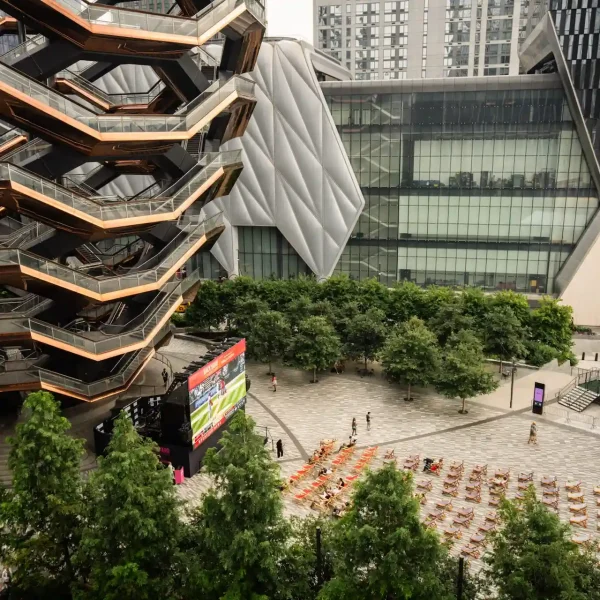 The Vessel and The Shed in Hudson Yards with lounge chairs and outdoor screen in vibrant urban plaza