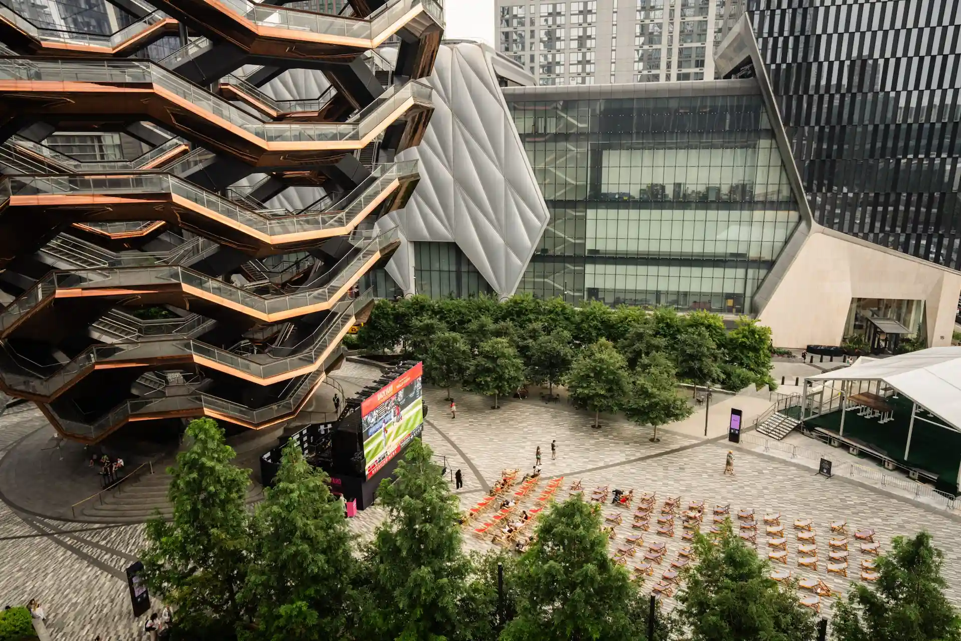 The Vessel and The Shed in Hudson Yards with lounge chairs and outdoor screen in vibrant urban plaza