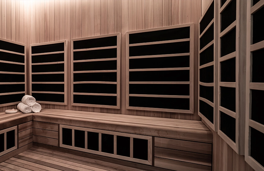 Interior of modern infrared sauna with light wood panels, heating slats, and rolled white towels on bench