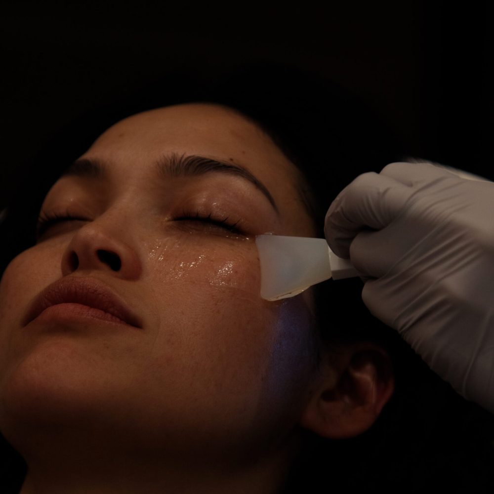 Close-up of facial skincare treatment with gloved hand applying gel using translucent spatula