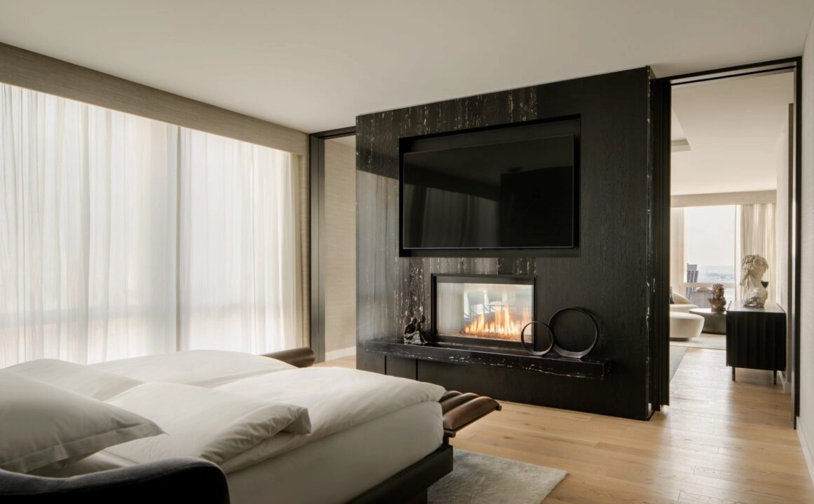 Modern bedroom with fireplace, TV, white bedding and sculptural decor in sunlit minimalist interior