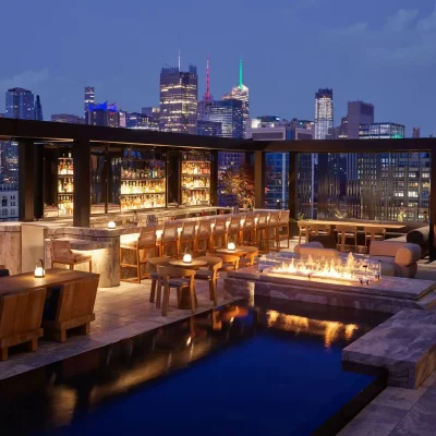 Rooftop bar at night with pool, fire pit, and city skyline, evoking vibrant urban luxury