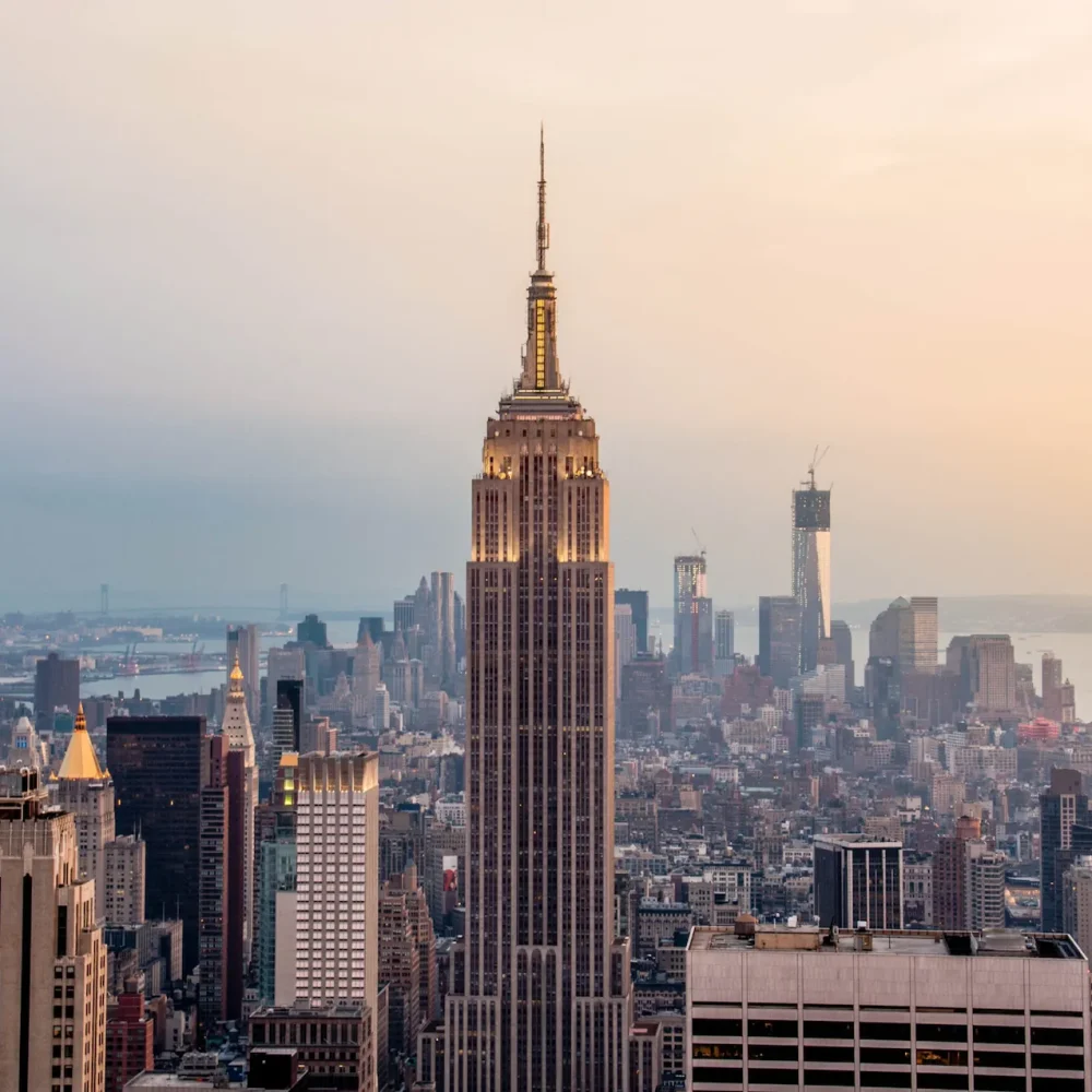 Empire State Building centered in Manhattan skyline at sunset with warm light and distant Hudson River
