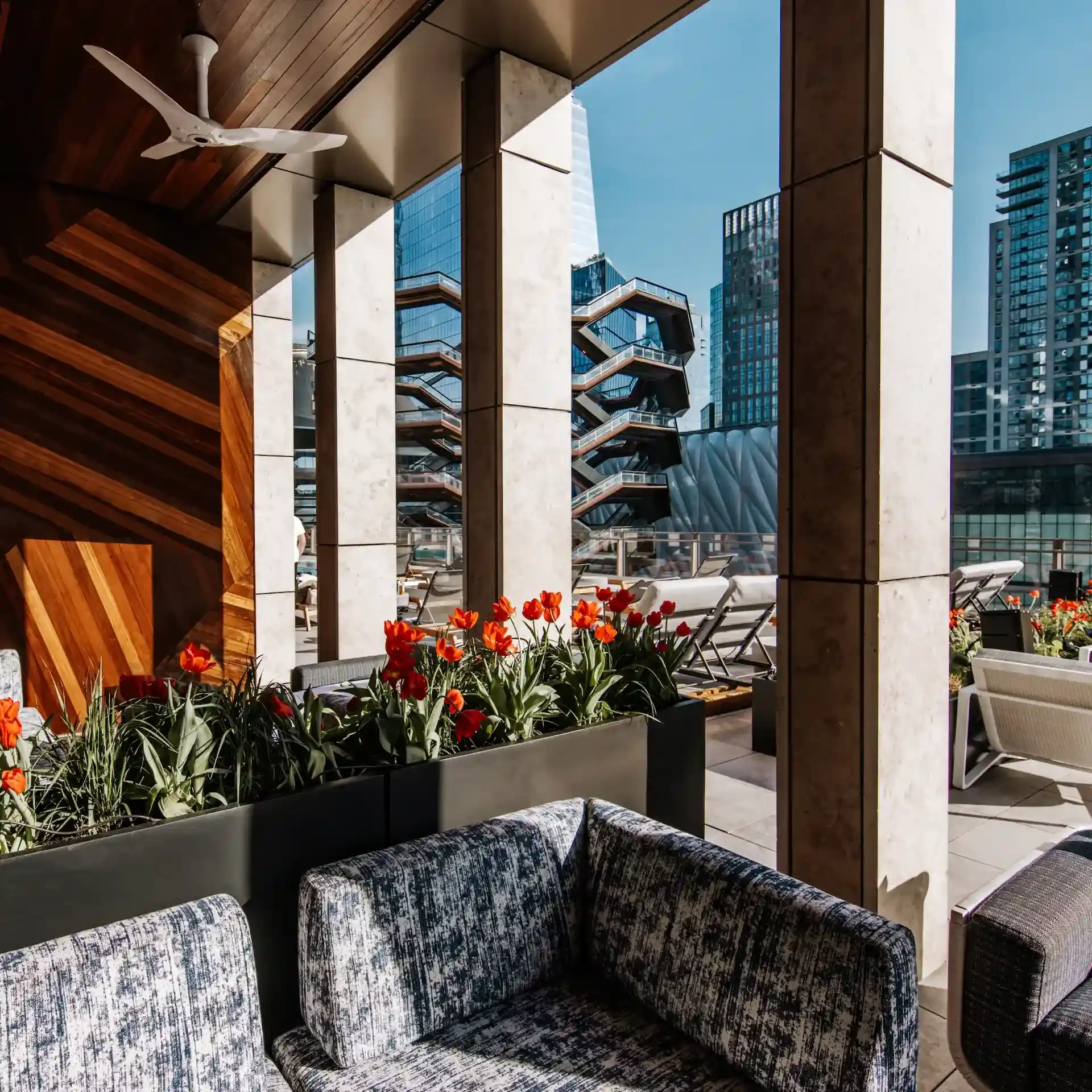 Outdoor lounge at Equinox Hotels with cushioned seating, red tulips, and view of the Vessel in Hudson Yards