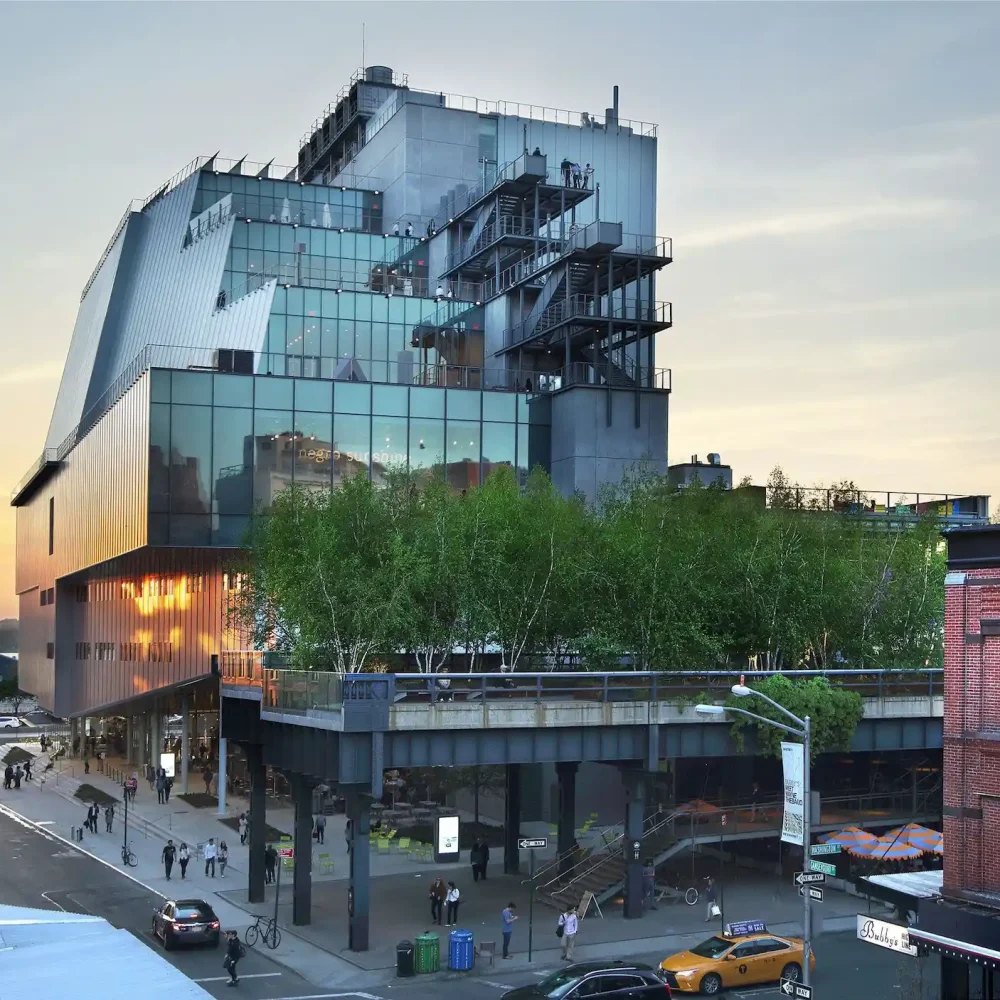 Whitney Museum at sunset with glass terraces, High Line trees, and street scene with yellow taxi